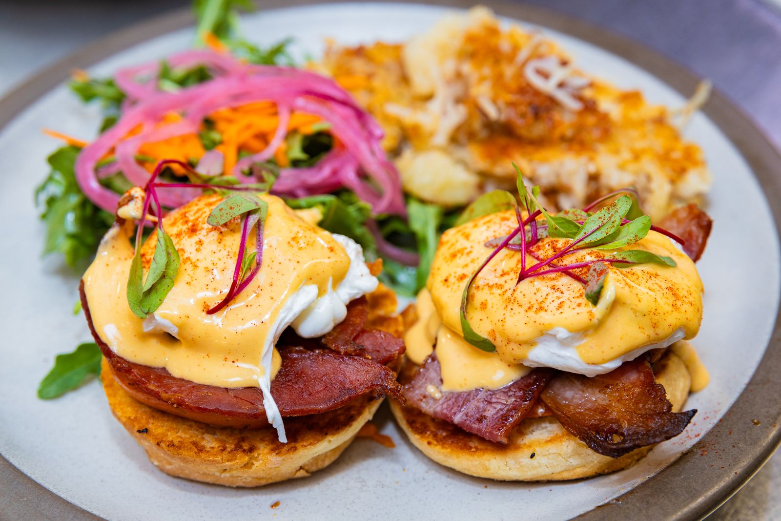 Two eggs Benedict on biscuits with bacon, hollandaise, and a side salad.