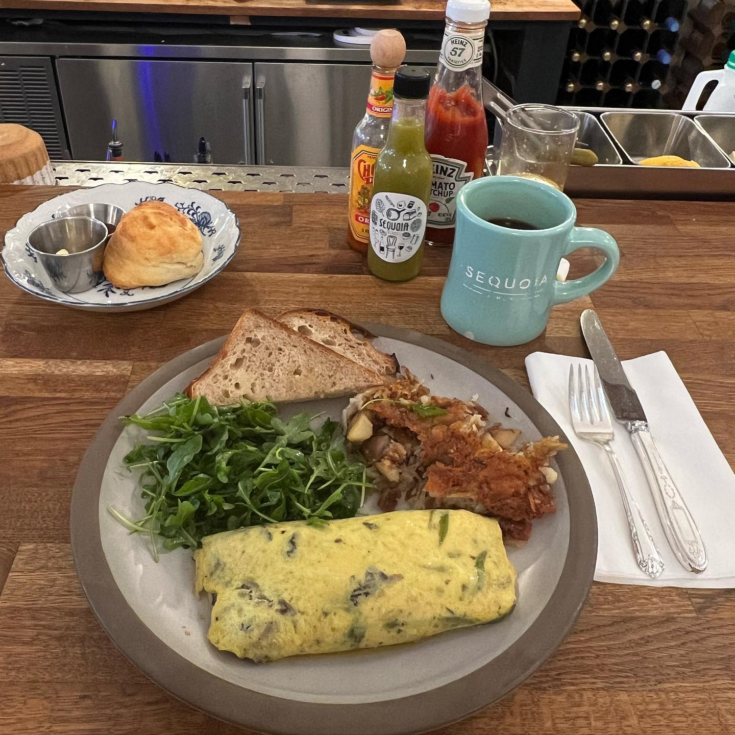 A table spread at Sequoia Diner with an omelet, toast, arugula, and coffee, with the bar and wine bottles in the background